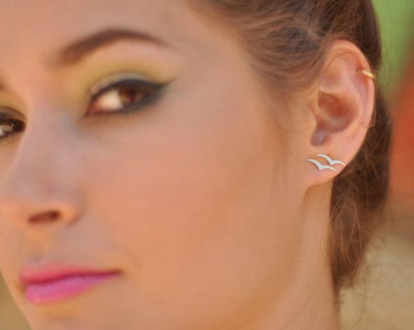 Small silver flying bird earrings attached to the ear