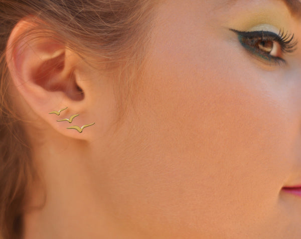 A trio of golden flying bird earrings attached to the ear