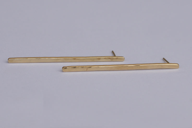 Long gold hammered bar earrings close to the ear