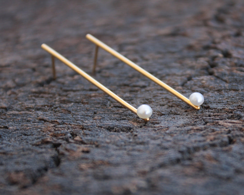 Long gold bar earrings with a pearl attached to the ear