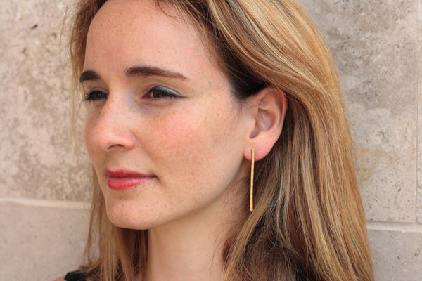 Long gold hammered bar earrings close to the ear