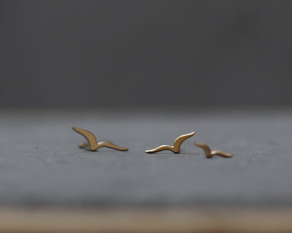A trio of golden flying bird earrings attached to the ear