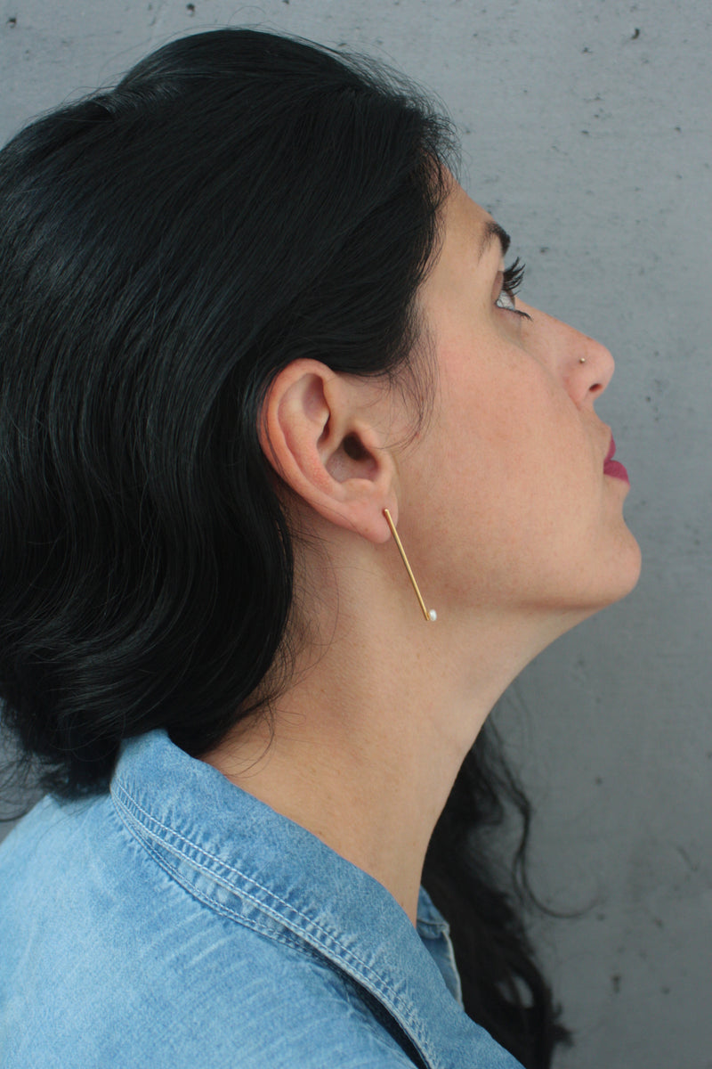 Long gold bar earrings with a pearl attached to the ear